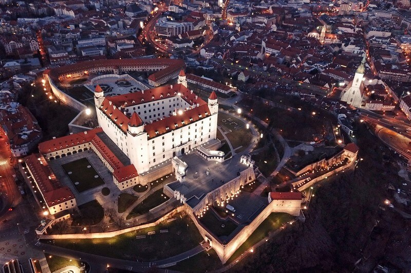 Aerial view of Bratislava Castle at dusk above the illuminated Old Town